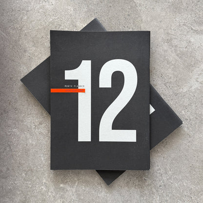 Two black 12-Month Planners stacked, the top one showing a large 12 and an orange stripe