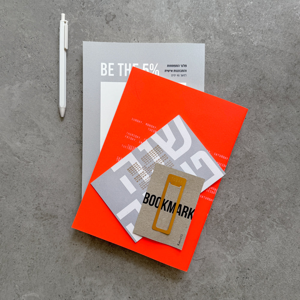 Flat lay of the BE THE 5% journal, orange notebook, gold Bookmark on its card, a Shana Tova card and a white gel pen