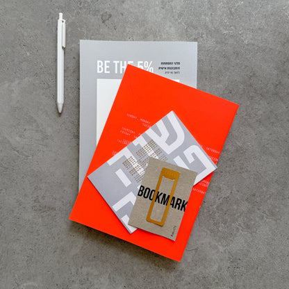 Flat lay of the BE THE 5% journal, orange notebook, gold Bookmark on its card, a Shana Tova card and a white gel pen