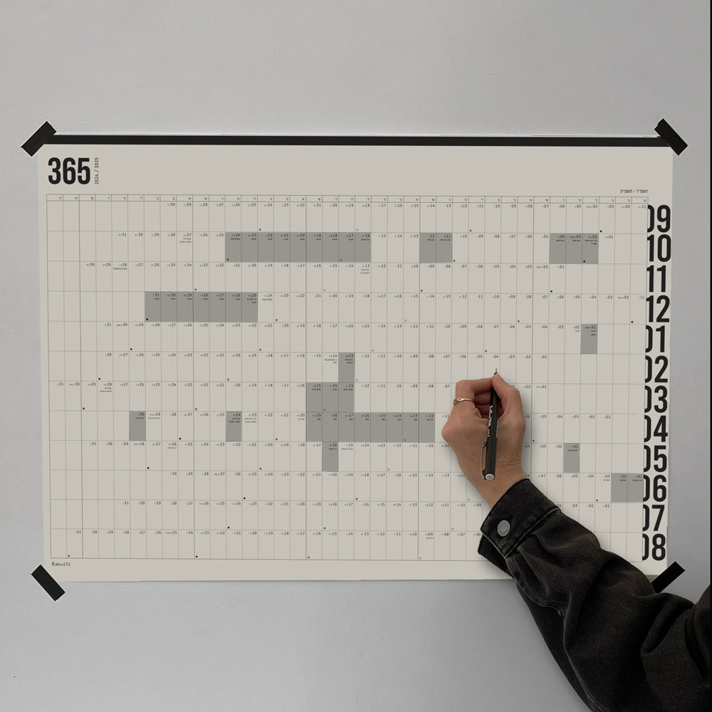 KaRiniTi 365 Day Yearly Planner – full wall poster view, all 12 months annual grid with Israeli holiday highlights, person writing