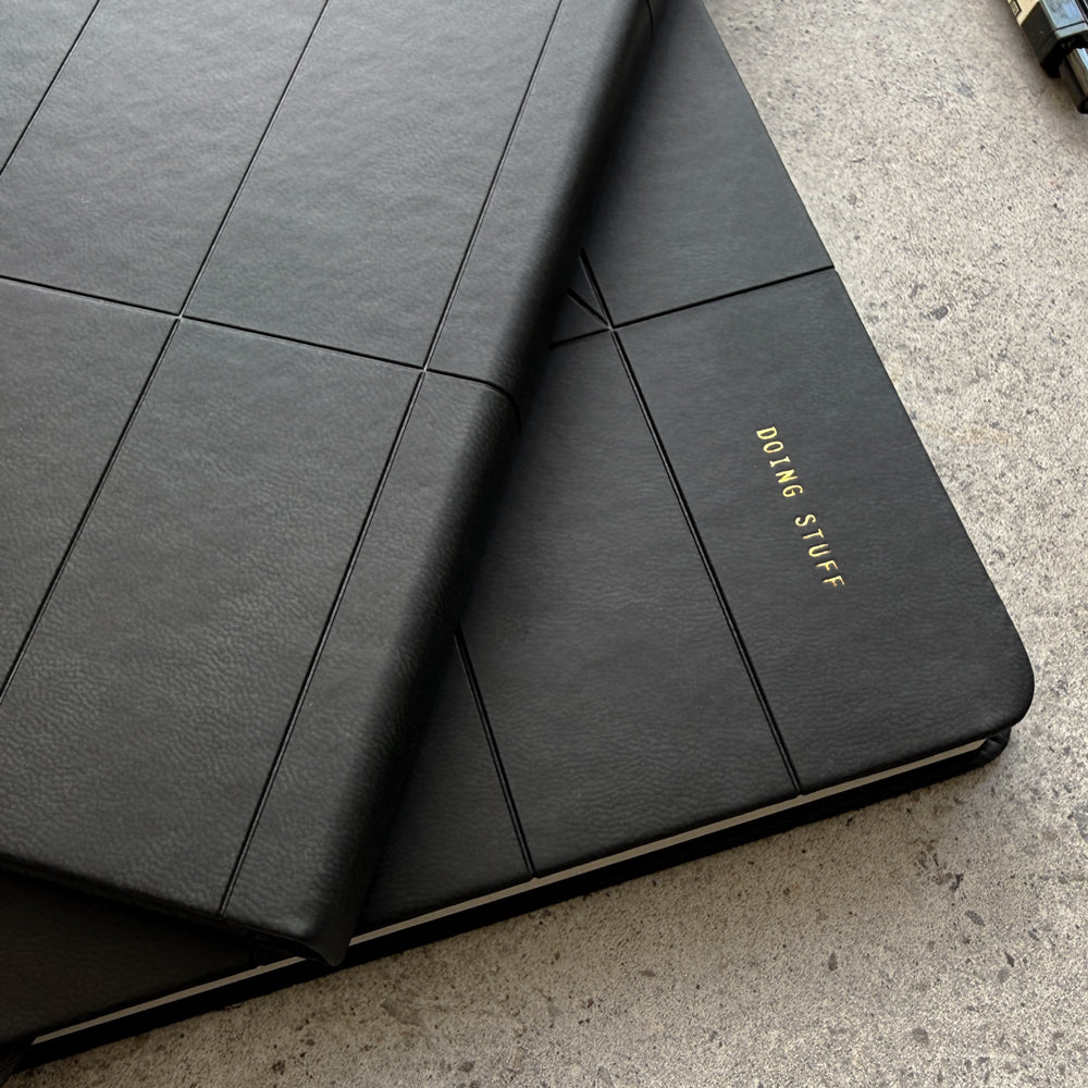Close-up of notebook corner showing Doing Stuff gold foil stamp on black PU cover