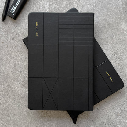 Black PU reversible hardcover notebook with embossed geometric line pattern, Write It Down gold foil stamp on top notebook and Doing Stuff stamp on flipped notebook below