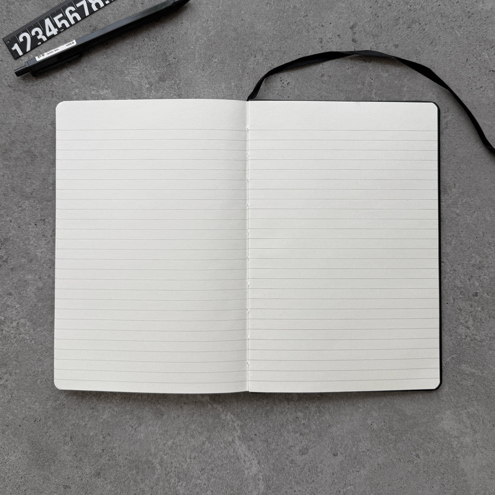Open black PU notebook showing lined cream interior pages and black ribbon bookmark