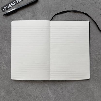 Open black PU notebook showing lined cream interior pages and black ribbon bookmark