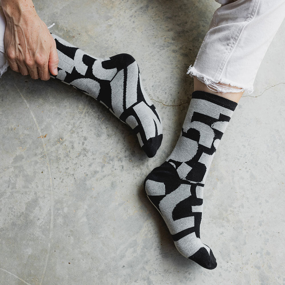 Elevate your everyday style with our elegant unisex socks designed by the KaRiniTi Studio. These monochromatic socks blend clean lines with subtle, refined details, echoing our passion for precision and typography. Perfect for any outfit, each pair brings a unique design element inspired by our studio's signature obsession with structured layouts and minimalist aesthetics.

- Numbers: Featuring bold, oversized numbers in various cuts, this design draws inspiration from KaRiniTi's signature wrapping paper. T