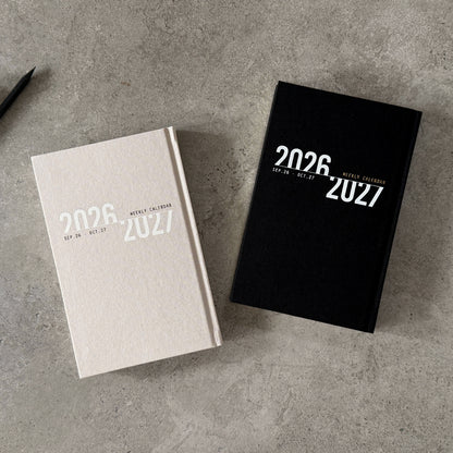 KaRiniTi Weekly Calendar 2026/2027 – grey and black covers together on concrete, Sep 26 – Oct 27